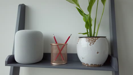 Slow-Motion-Panning-Shot-of-Man-Tapping-an-Apple-HomePod-on-top-of-Modern-Looking-Bookshelf-adjacent-to-a-Pencil-Holder---Plant