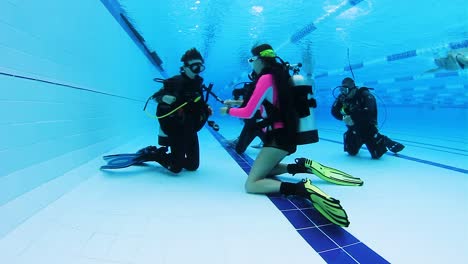 A-female-scuba-instructor-teaching-a-young-child-and-mother-how-to-scuba-dive-in-a-pool