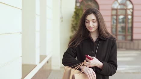 Caucasian-Female-Walking-Down-The-Street-With-Few-Bags-After-Shopping-Spinning-and-Looking-at-The-Camera-Holding-Her-Smartphone