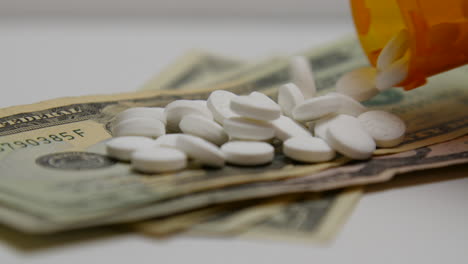 Pill-bottle-pours-out-white-pills-onto-stacks-of-money
