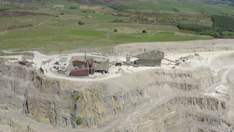 An-aerial-view-of-a-working-asphalt-quarry-building-with-the-quarry-cut-in-the-foreground-and-countryside-in-the-background,-Yorkshire,-UK