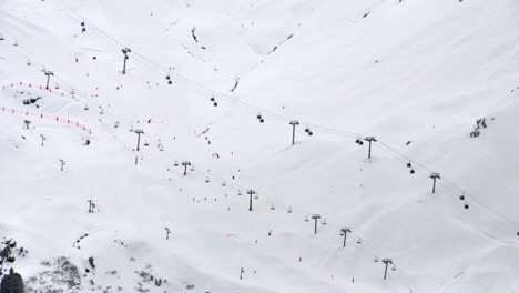 Time-lapse-of-2-ski-lifts-on-the-side-of-a-mountain-with-people-skiing-underneath,-in-the-resort-of-Meribel-in-the-French-Alps-in-winter
