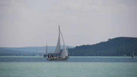 Sailboat-at-Lake-Balaton-with-Tihany-and-the-viaduct-of-Kőröshegy-in-the-background,-filmed-in-180-fps-slow-motion-at-Balatonfüred