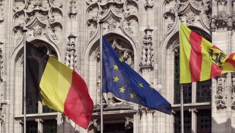 Mechelen,-EU-and-Belgian-flag-waving-in-front-of-Emperor-Charles-V-statue-on-the-town-hall-of-Mechelen,-SLO-MO