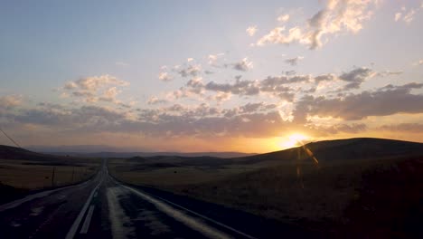 View-from-inside-car-on-empty-hilly-road-leading-to-horizon-line-at-sunset-or-sunrise