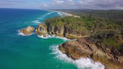Aerial-view-of-wild-coastline-with-cliffs,-forest,-turquoise-blue-water-and-waves-splashing