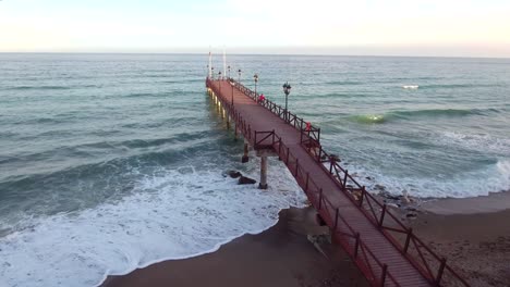 drone-shot-of-wooden-pier-in-the-sea,-filmed-in-marbella,-malaga,-spain