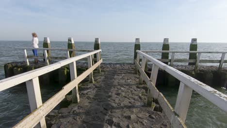 A-woman-walks-along-a-small-pier-with-a-wooden-railing