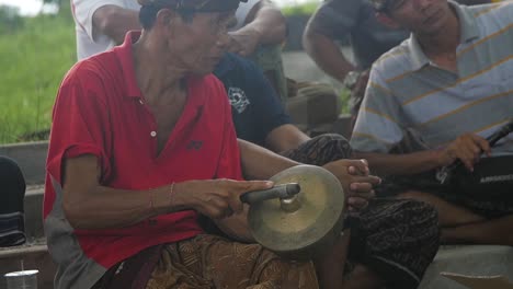Slow-motion-panning-up-view,-Balinese-musicians-sitting,-playing-gold-percussion-instruments-in-groups-together