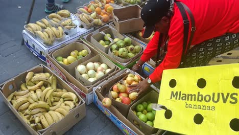 An-African-american-woman-street-vendor-bagging-fruit-for-a-customer-on-a-street-market-in-central-Cape-Town