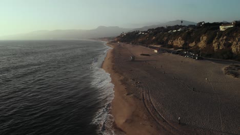 Eine-Ariel-aufnahme-Eines-Strandes-In-Der-Nähe-Von-Point-Dume-Cliff-In-Malibu-In-Kalifornien,-Während-Die-Wellen-Abends-Bei-Sonnenuntergängen-Auf-Den-Sand-Rollen
