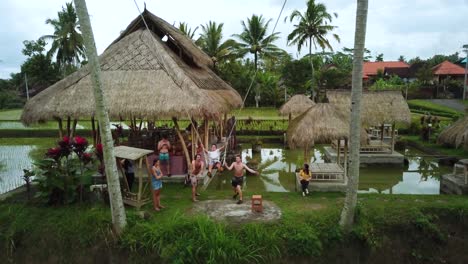 Drohnenaufnahme-Eines-Touristen,-Der-Eine-Schaukel-Zwischen-Zwei-Kokospalmen-Genießt,-Die-über-Einige-Reisterrassen-In-Bali,-Indonesien,-Schwingt