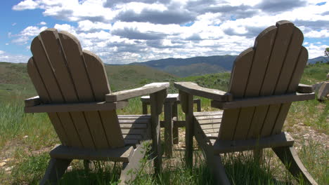 A-shot-of-two-wooden-lawn-chairs-overlooking-a-vast-view-of-the-mountains