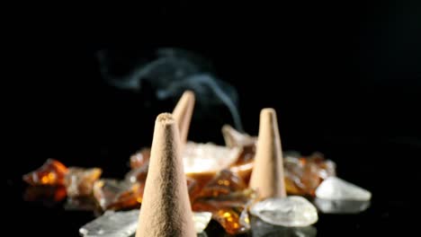 Slowly-pushing-past-several-unlit-incense-cones-in-a-decorative-rock-garden,-towards-a-lit-cone-with-smoke-billowing
