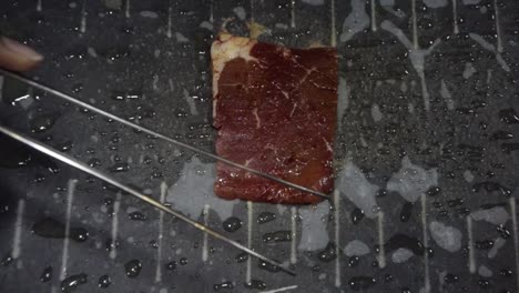 Thin-slice-of-beef-placed-and-cooked-on-hot-stone-barbecue,-closeup-slow-motion