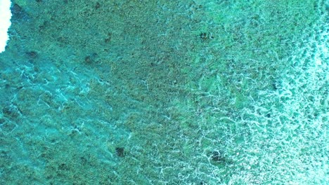 Weiße-Welle,-Die-Sich-über-Korallenriffe-In-Der-Nähe-Der-Küste-Der-Tropischen-Insel-Ausbreitet-Und-Eine-Wunderschöne-Meerestextur-Von-Oben-Erzeugt