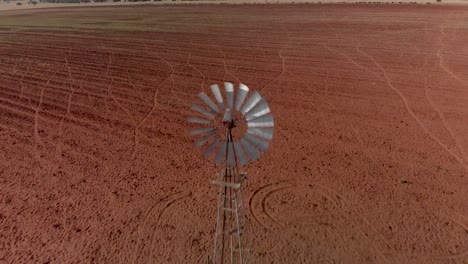 Aerial-Reverse-Dolly,-Der-Eine-Funktionierende-Windpumpe-Auf-Einem-Bauernhof-Mit-Gepflügtem,-Ungenutztem-Land-Enthüllt