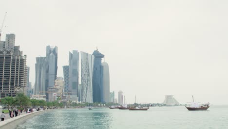 Menschen,-Die-An-Der-Corniche-Mit-Dau-booten-Und-Der-Skyline-Von-Doha-Spazieren-Gehen