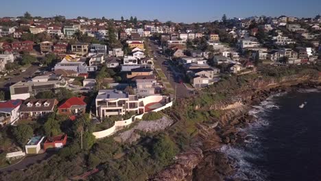 Beautiful-reverse-drone-shot-of-houses-near-the-beach-and-cliff-with-view-of-pacific-ocean-waves-crashes-the-rocks