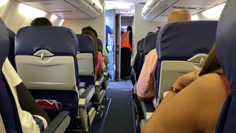 Airplane-cabin-with-passengers,-crewman-in-orange-vest-briefing-pilots-in-cockpit