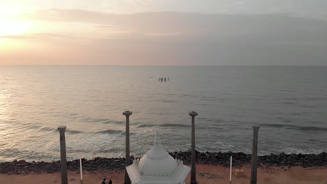 Aerial-Reveal-Shot-of-Mahatma-Gandhi-Statue-from-the-Beach-on-a-Golden-Sunrise-in-the-morning-near-Pondicherry-Rock-Beach,-shot-with-a-drone-in-4k