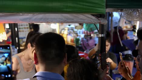 Group-of-people-recording-beautiful-hot-woman-on-street-food-market-stall,-Thailand