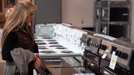 Pretty-mature-blonde-woman-turning-the-knobs-on-a-stove-at-a-kitchen-appliance-store
