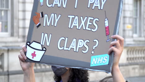 Ein-Demonstrant-Hält-Ein-Plakat-Hoch,-Auf-Dem-Steht:-„Kann-Ich-Meine-Steuern-In-Klatschen-Bezahlen?