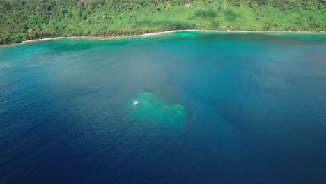 Aerial-Approaching-View-To-Boat-Anchored-Over-Underwater-Cliff-in-Tropical-Sea-by-Exotic-Island