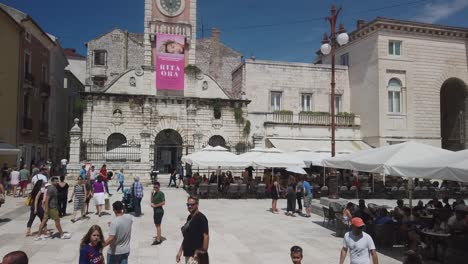 Busy-restaurants-and-shops-at-the-bell-tower-in-People's-Square,-Zadar