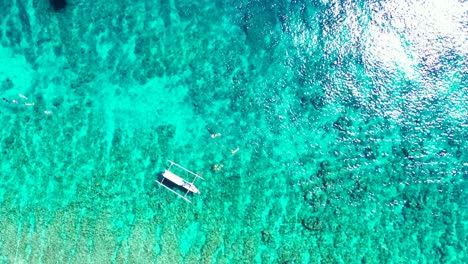 perfectly-clear-turquoise-seawater-and-healthy-coral-reef,-tourists-snorkeling-and-exploring-rich-marine-life,-tropical-ocean-with-tour-boats-floating-on-the-calm-water
