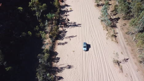 Aerial,-offroad-car-driving-on-dry-sandy-river-bed-in-remote-bushland,-tilt-down