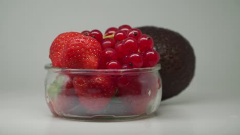 Ripe-Avocado,-Strawberries-And-Red-Currants-In-A-Clear-Glass-Bowl-Rotating--Close-Up-Shot