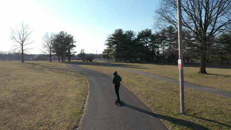 An-aerial-tracking-of-a-man-on-an-electric-skateboard-in-an-empty-park-on-a-sunny-day