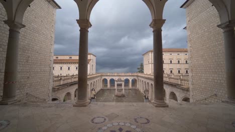 Looking-through-tall-arches-at-outdoor-courtyard-in-abbey-of-Montecassino-on-stormy-cloudy-day,-Italy,-handheld-pan