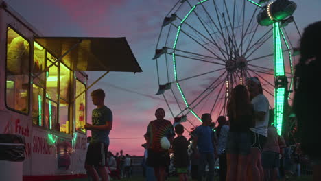 Young-boy-buying-food-from-stand-at-small-carnival-at-dusk,-Wide-Shot