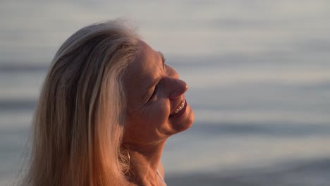 Beautiful-mature-blonde-woman-with-gray-hair-on-a-beach-smiling-and-looking-into-the-setting-sun