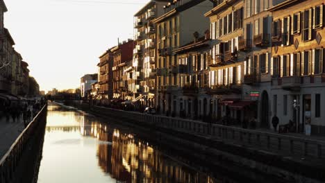 Naviglio-Grande-canal-in-Milan-Italy-at-sunset-with-the-famous-buildings-shining-in-the-sunlight,-slow-pan-wide-shot-handheld