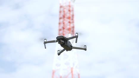 Drone-Flotando-Y-Volando-En-El-Aire-Con-Cielo-Azul-Brillante-Y-Torre-De-Transmisión-En-El-Fondo
