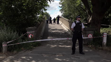 A-police-officer-stands-guard-at-a-taped-off-police-cordon-as-a-forensics-team-investigates-a-bridge-following-a-gun-and-knife-crime-incident