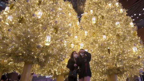 Frauen-Feiern-Die-Weihnachtsfeiertage,-Indem-Sie-Ein-Selfie-Vor-Einem-Goldenen-Weihnachtsbaum-In-Einem-Einkaufszentrum-In-Hongkong-Machen