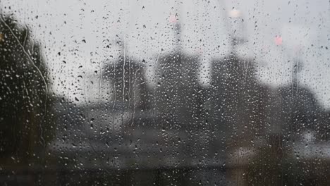 Regentropfen-Fallen-Auf-Das-Fenster-Mit-Verschwommenen-Baukränen-Im-Hintergrund