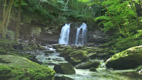A-young-man-and-woman-sit-beside-Seneca-Falls,-a-large-waterfall-located-along-Seneca-Creek,-within-the-Spruce-Knob-Seneca-Rocks-National-Recreation-Area-in-West-Virginia