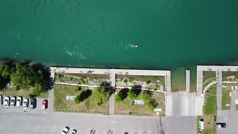 Aerial-top-down-shot-of-parking-cars-beside-river-with-person-paddling-on-sup-board-during-sunny-day-in-Canada