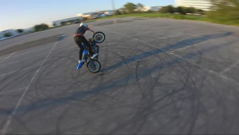 Stunt-biker-does-a-trick-while-spinning-on-one-wheel,-captured-with-an-FPV-drone-chasing-it