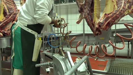 Employee-cleaning-horse-meat-hung-in-slaughterhouse-with-knife