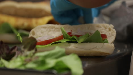 Person-In-Handschuhen,-Die-Thunfischsandwich-Mit-Frischem-Gemüse-Zubereitet-Und-Zubereitet