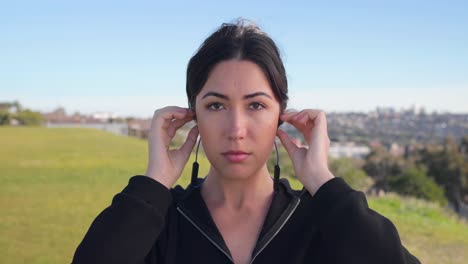 Eurasian-female-puts-headphones-in-before-going-for-a-run-looking-at-camera