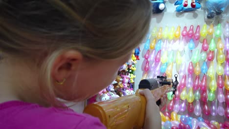 Junges-Kaukasisches-Mädchen,-Das-Gummigewehr-Auf-Reihen-Bunter-Luftballons-Schießt,-Um-Preise-Am-Schießstand-Zu-Gewinnen