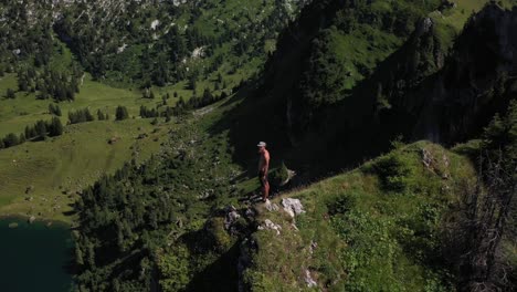 A-young,-fit-and-strong-man-is-standind-alone-by-himself-on-the-edge-of-a-cliff,-controlling-his-drone-and-looks-up-to-enjoy-the-view-during-the-hot-sunny-day-in-Seebergsee,-Switzerland